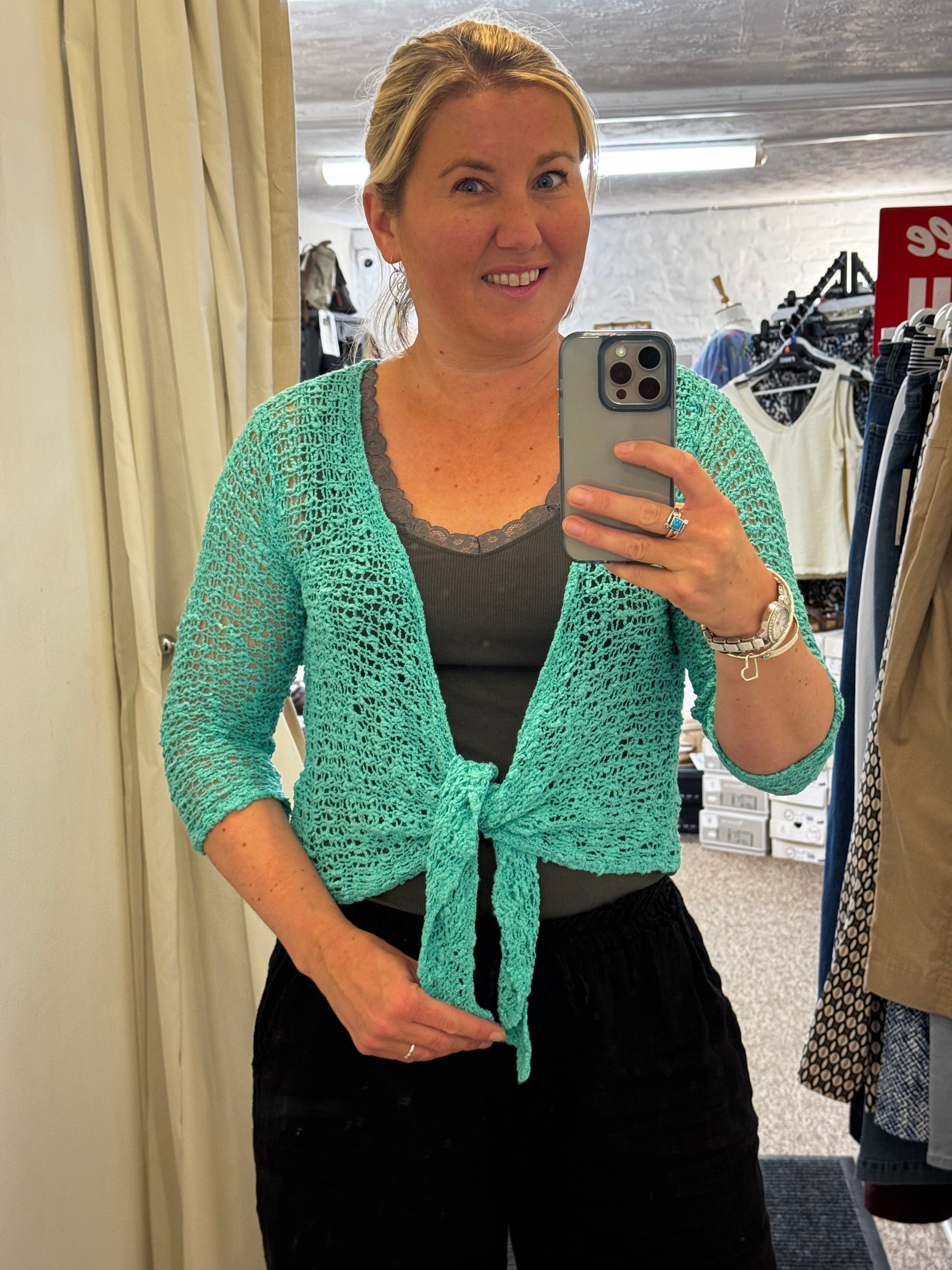 Woman taking a mirror selfie wearing a green knitted IKAT cardigan in The Coastal Boutique