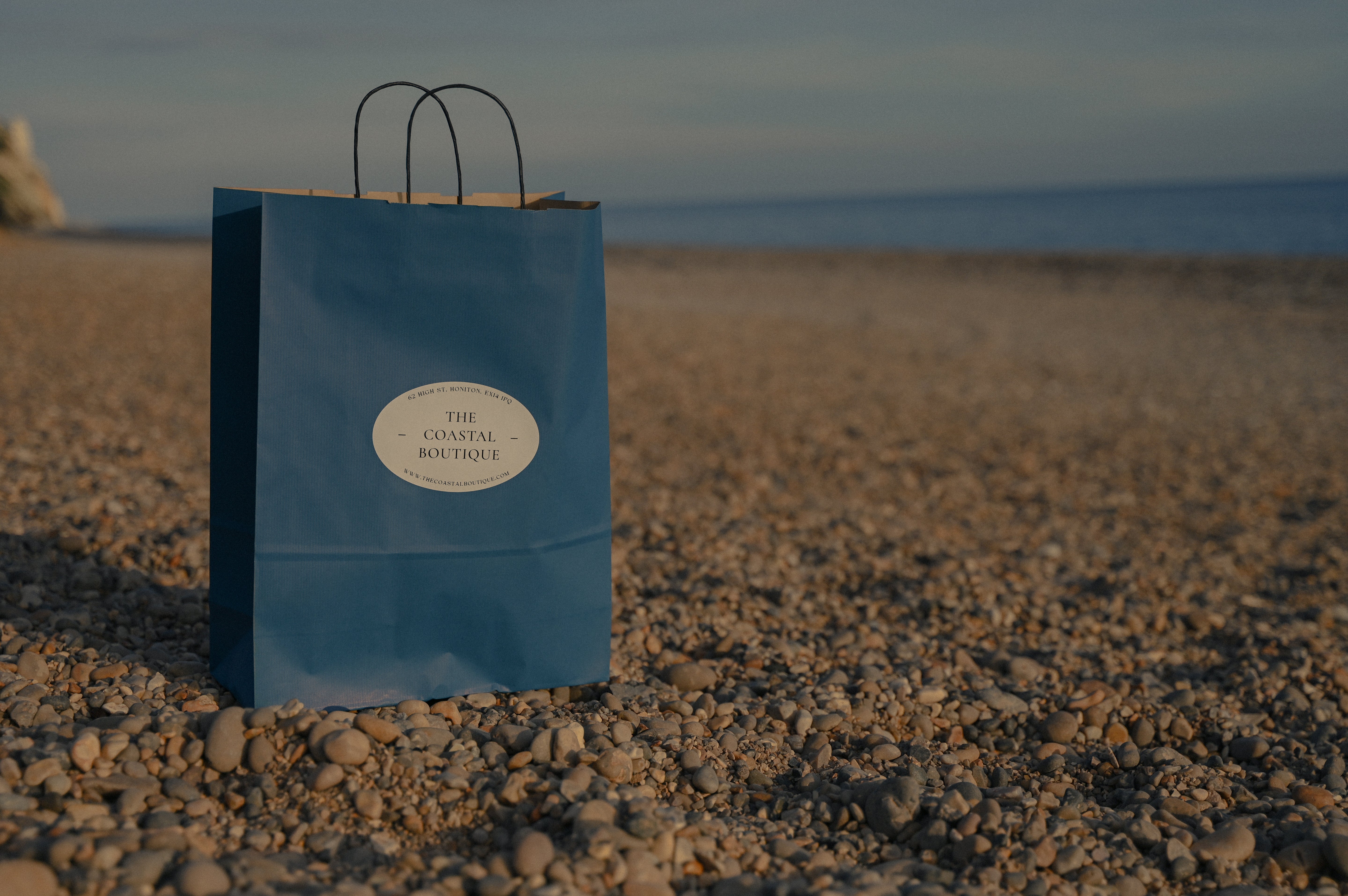 Blue paper bag with a label on a pebbly beach