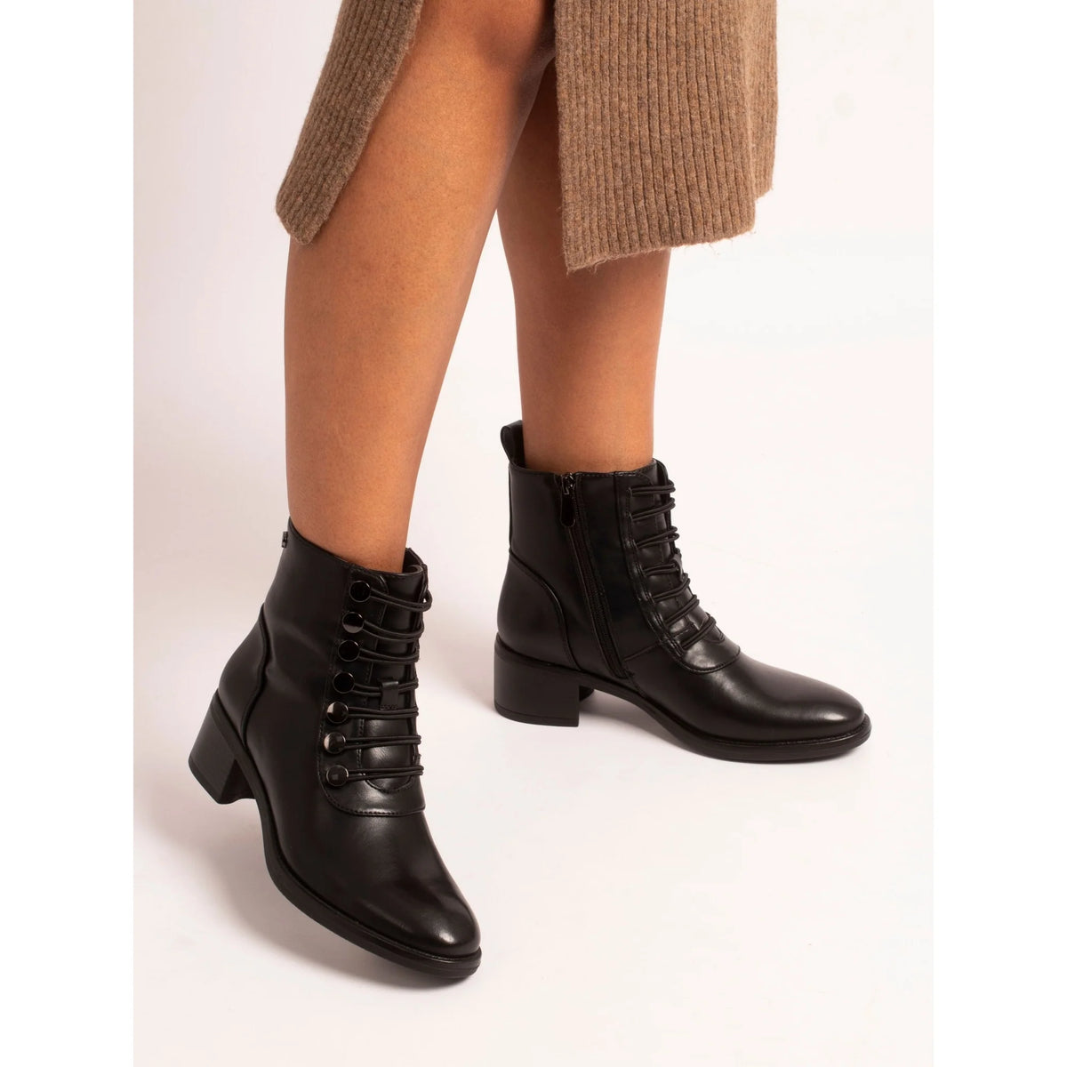 Black leather boots worn with a beige sweater on a light background